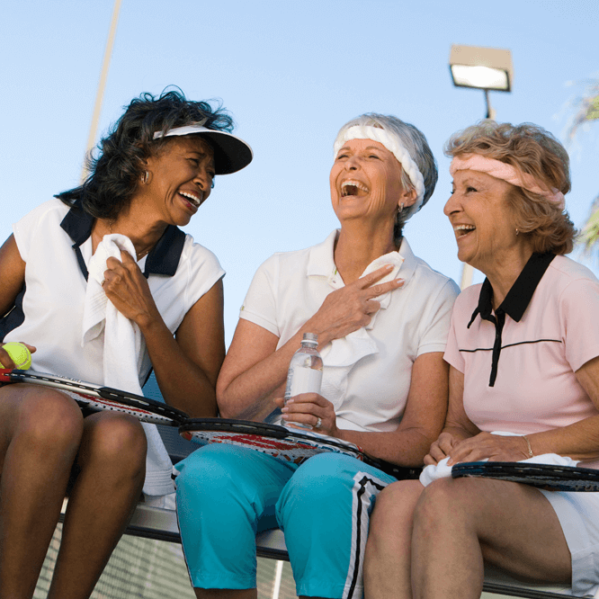 Three women laughing on the tennis court in an independent living community